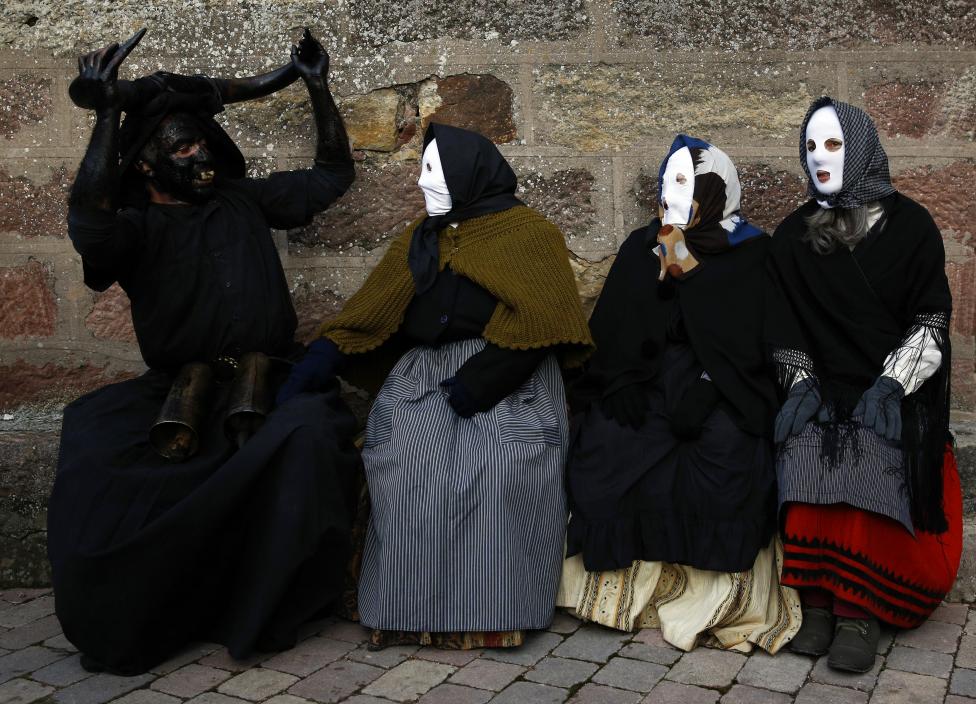 a reveller dressed as a "diablo de luzon" (luzon devil) sits next to others dressed as mascaritas" during carnival celebrations in luzon