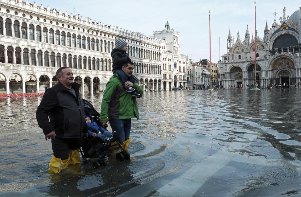 men carry children through a flooded st. mark's square during a period of seasonal high water in venice
