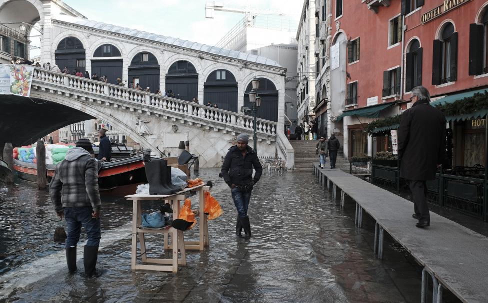 a man sells wellington boots in flood waters near rialto bridge during a period of seasonal high water in venice