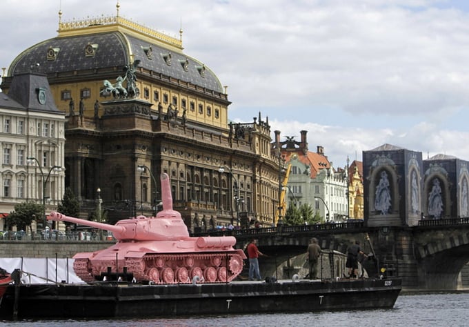 a soviet ww ii tank painted pink is located on a boat in front of the national theatre in prague