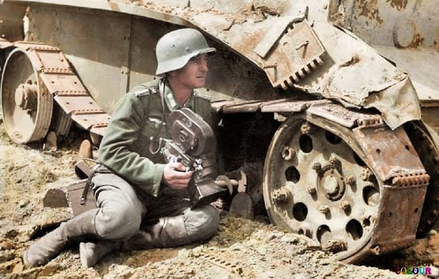 a kriegsberichter (war correspondent) holding an arriflex 35 2 1942 camera 35mm acr 0292 and he is leaning against a knocked out soviet bt-5 light tank. c.1940/41. (colorized by royston leonard from the uk)