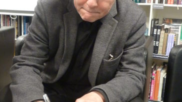 a man sitting at a desk in front of a book shelf