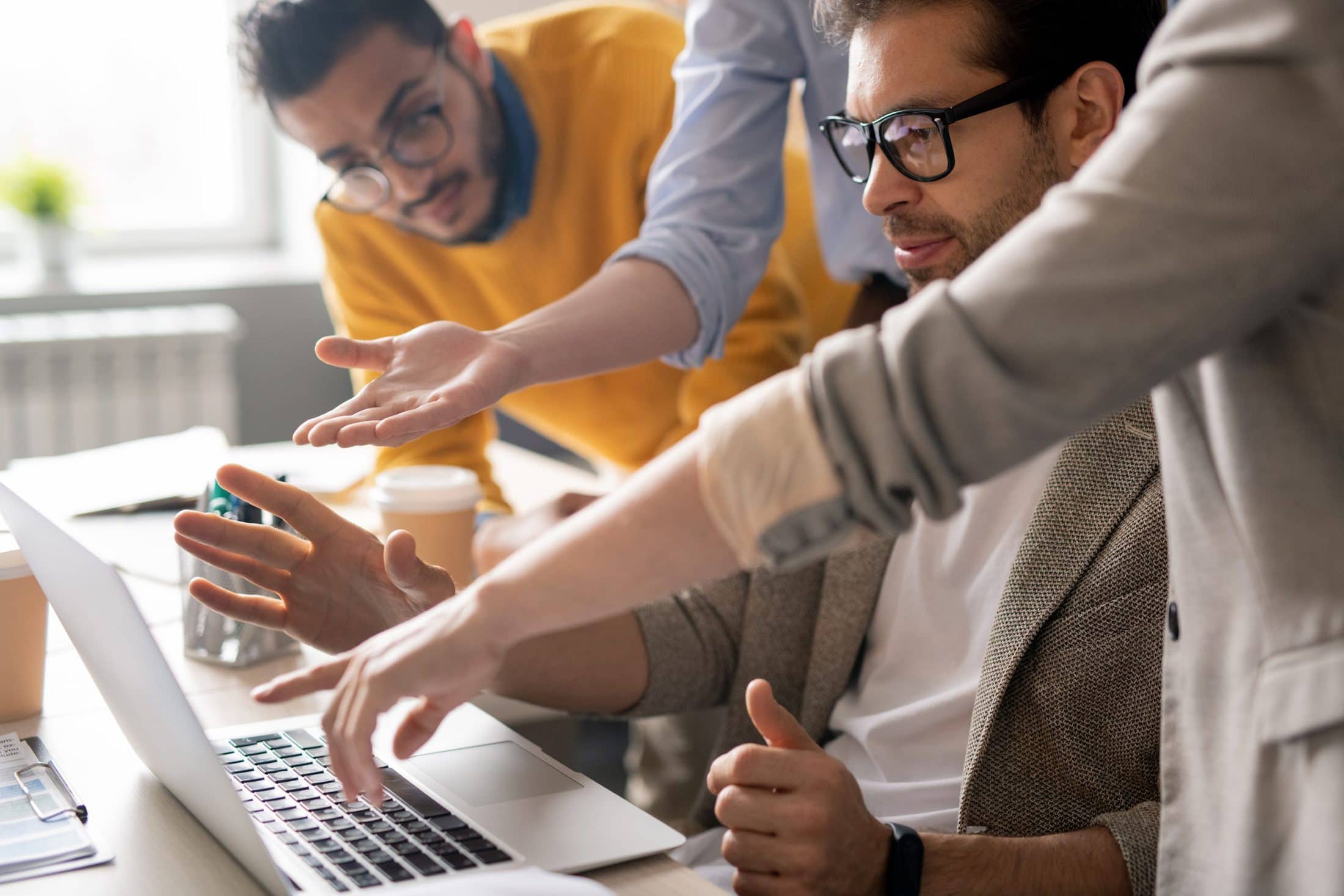 group of serious young business specialists pointing at laptop monitor and discussing web design in office