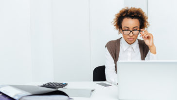 concentrated african american young woman accountant in glasses working in office using laptop