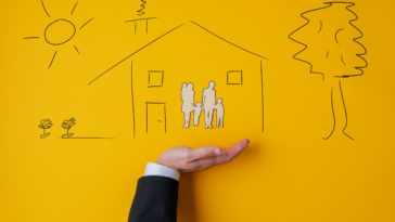 male hand in a suit in supportive gesture under a hand drawn house with a paper cut silhouette of a family inside in conceptual image. over yellow background.