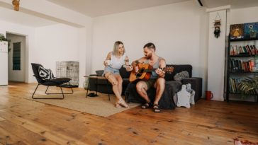 man sitting and playing acoustic guitar near woman in living room