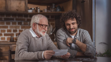 adult son and senior father looking at old photos at home