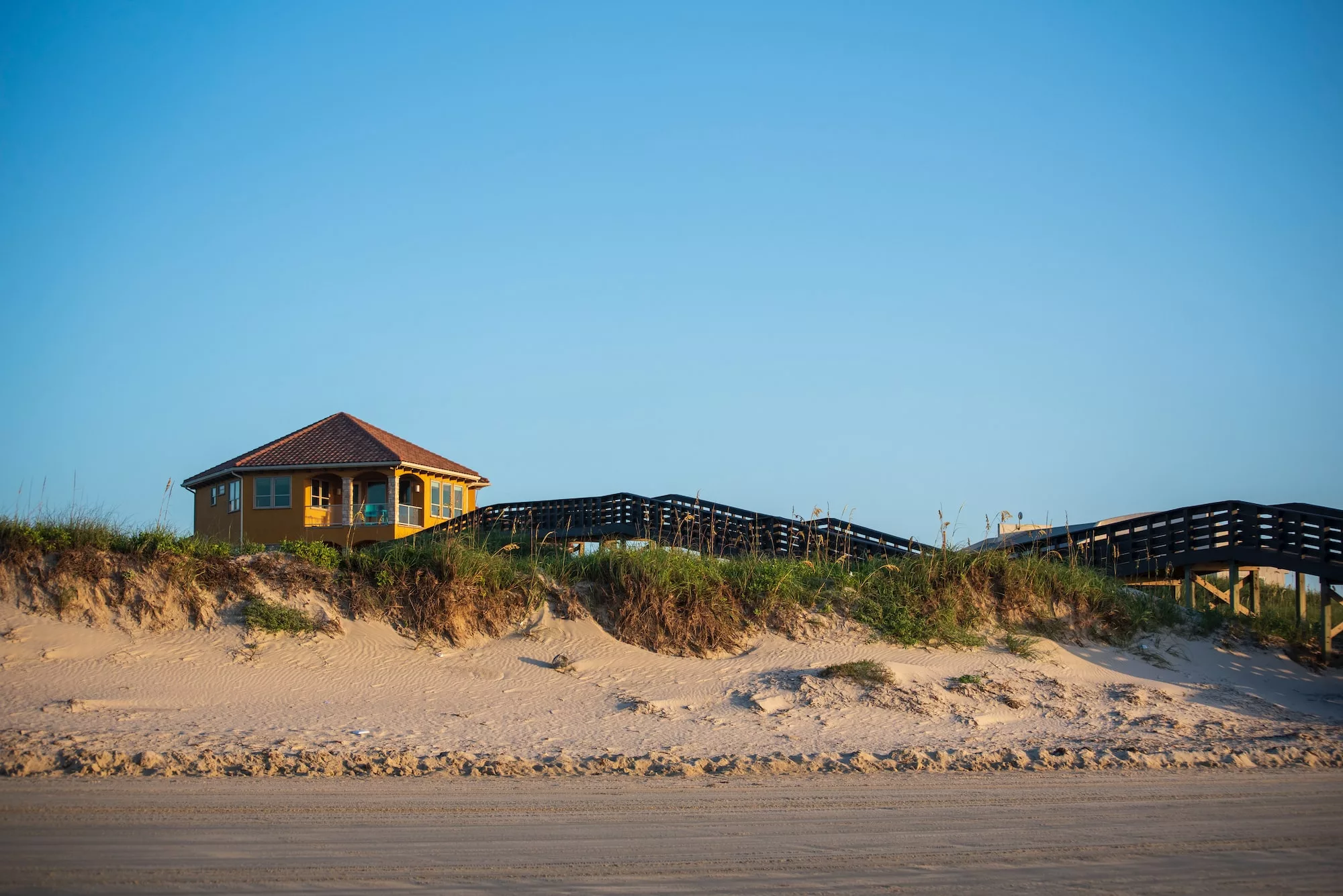 brown wooden house on brown sand near sea during daytime