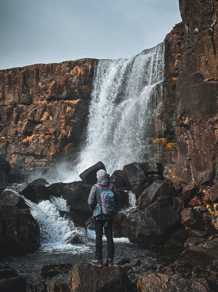 person standing near waterfall in pingvellir in iceland