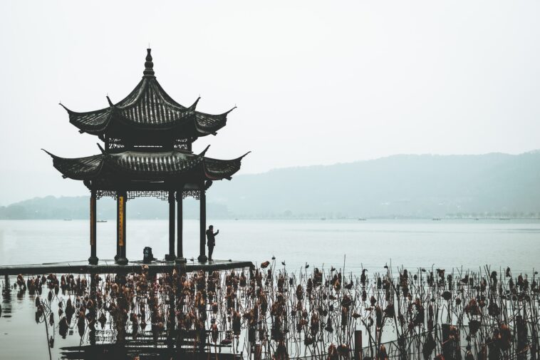 a group of people standing next to a body of water with west lake in the background