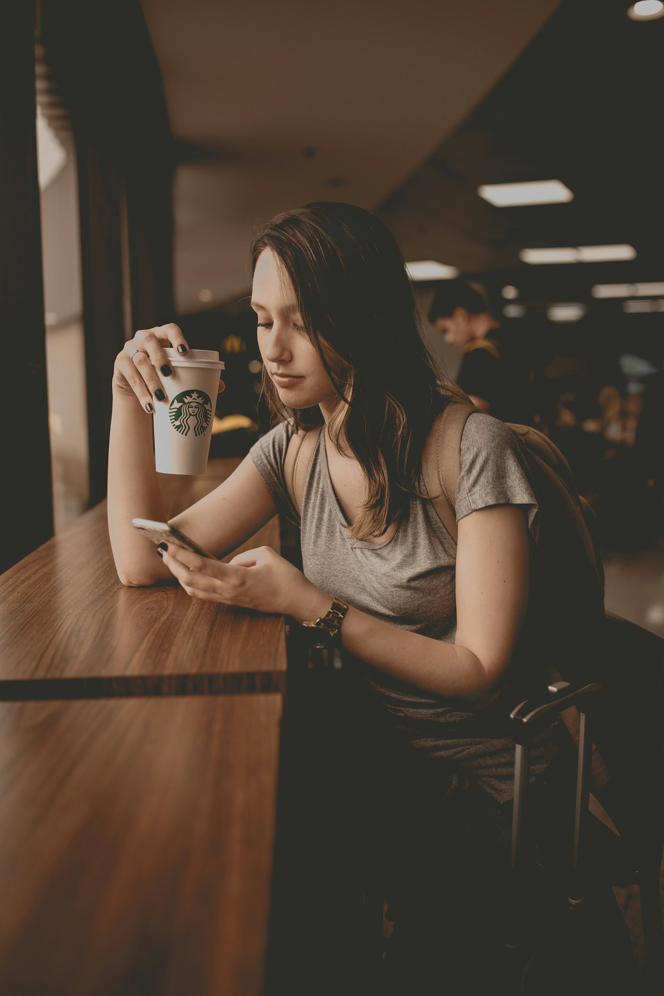 Economical Elegance: The Traveller’s Guide to Cost-Effective Airport Accommodations woman holding starbucks disposable cup and smartphone