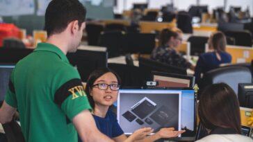 woman sitting in front of computer monitor explaining something two man and woman beside her