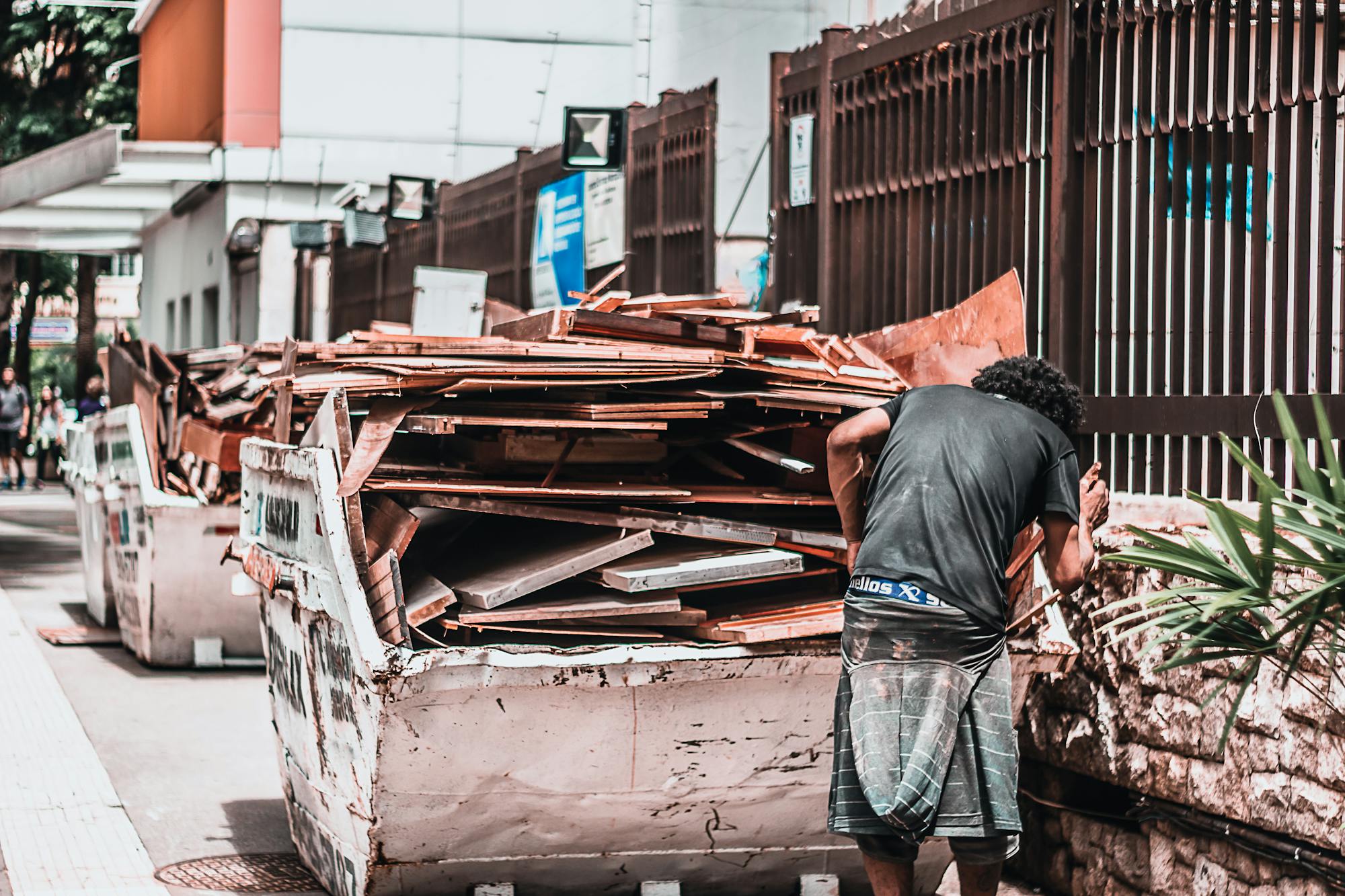 Why Renting a Dumpster is Better Than Multiple Trips to the Landfill man collecting materials from a waste container in an urban street, emphasizing recycling and waste management.
