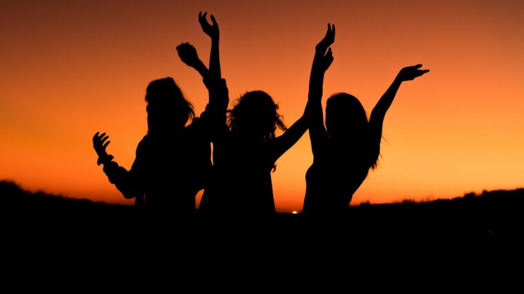 silhouette of three woman with hands on the air while dancing during sunset