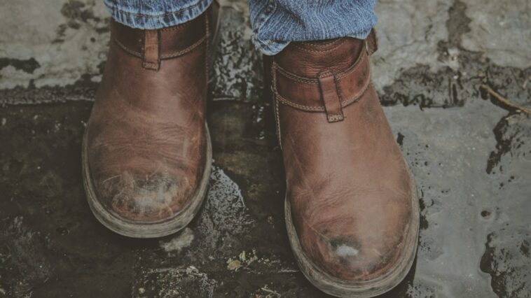 person in brown leather boots on grey concrete pavement