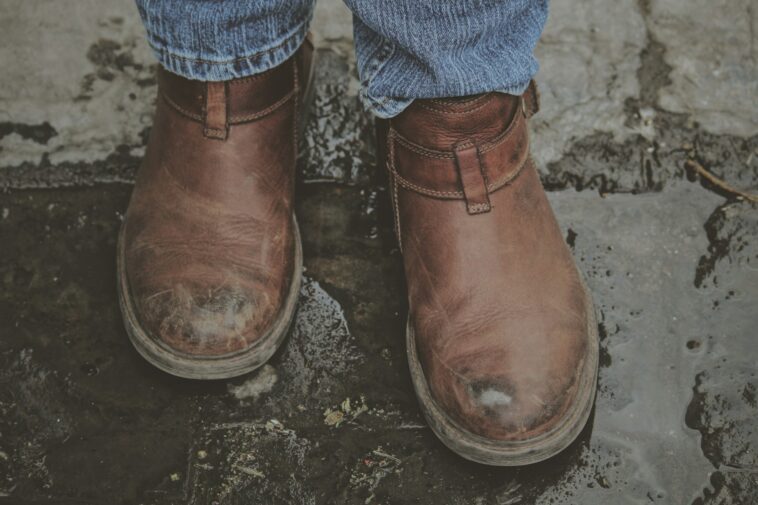 person in brown leather boots on grey concrete pavement