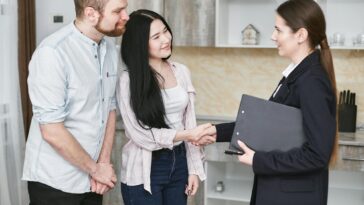 a young couple shakes hands with a real estate agent during a home tour or negotiation in a modern setting.